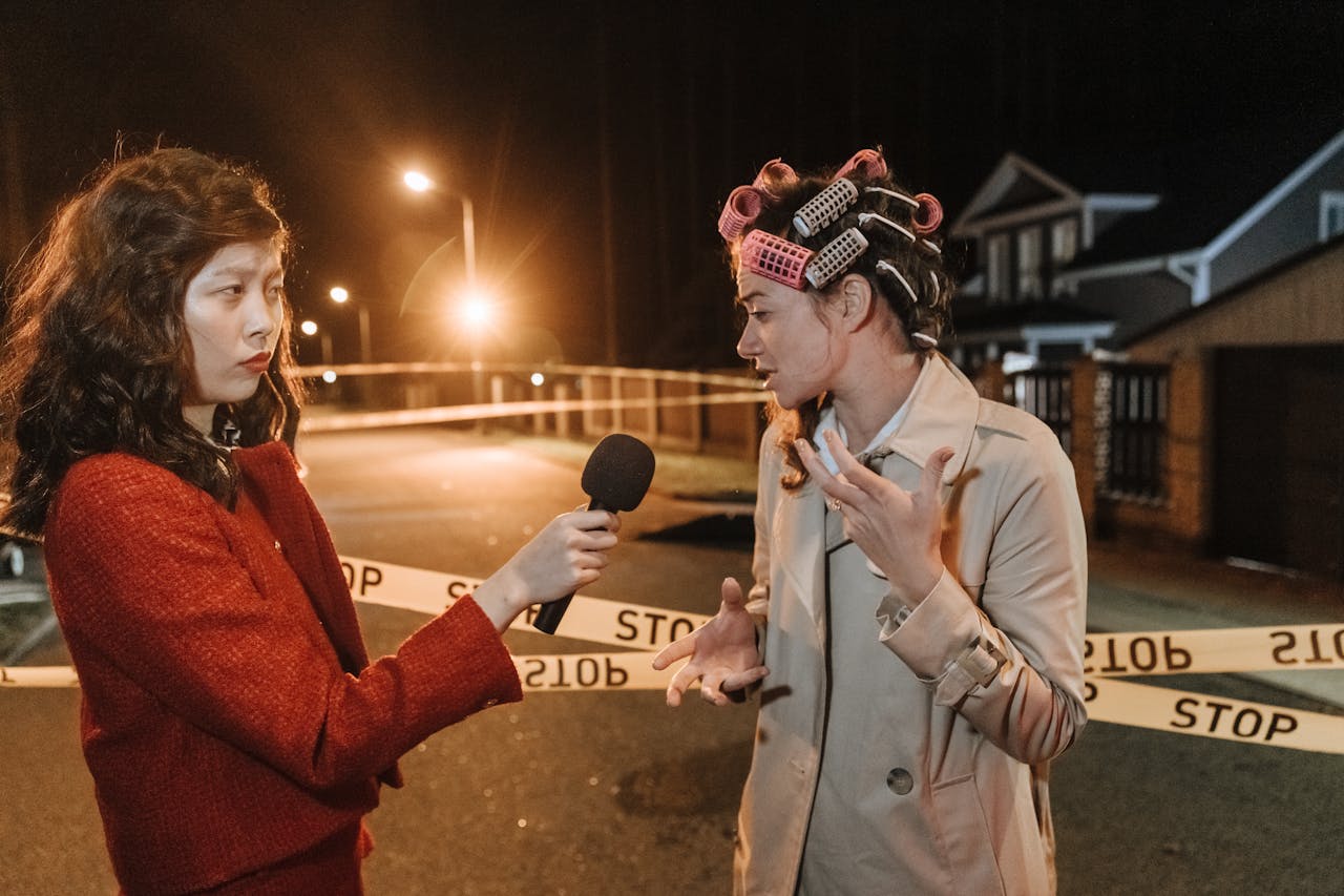 about-us Asian female journalist interviews a woman at a night crime scene. Police tape marks the area.