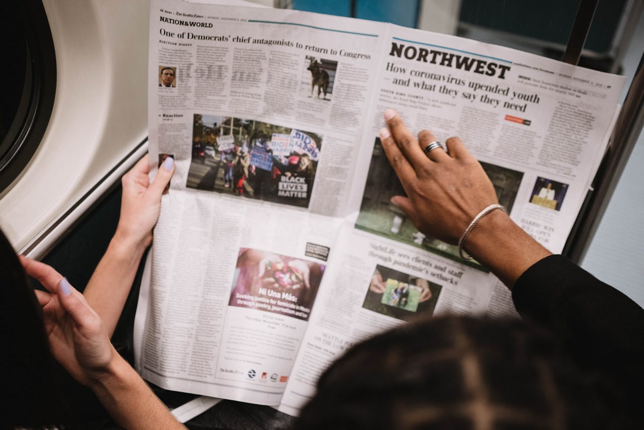 about-us People reading a newspaper on a subway train, highlighting current events and diverse perspectives.