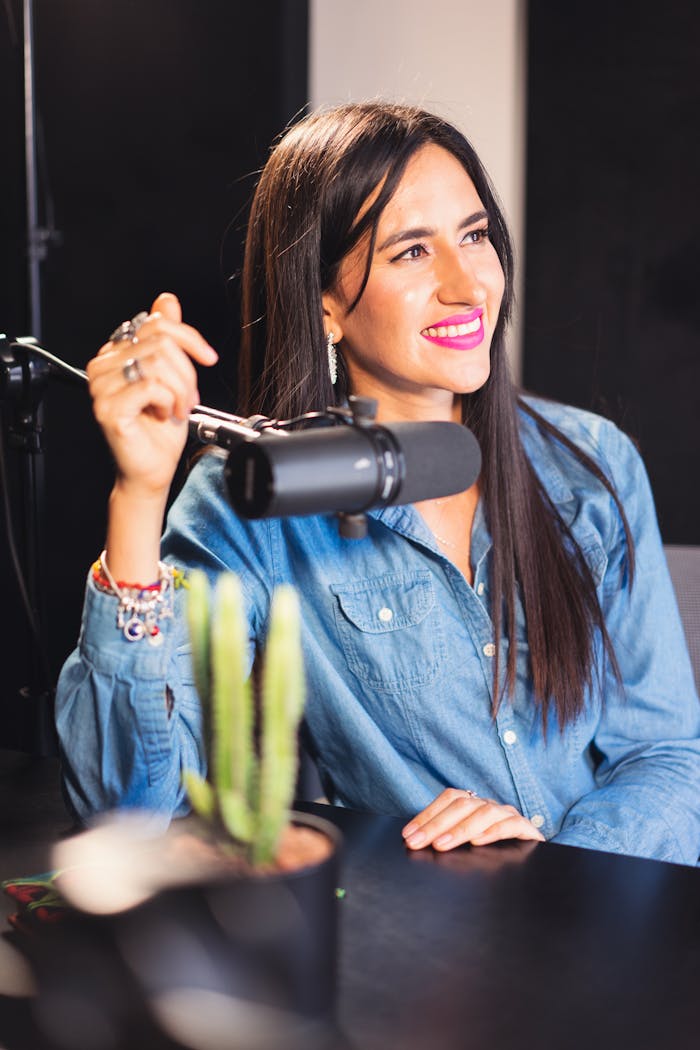 our-story Cheerful woman podcast host in recording studio with microphone and denim shirt.