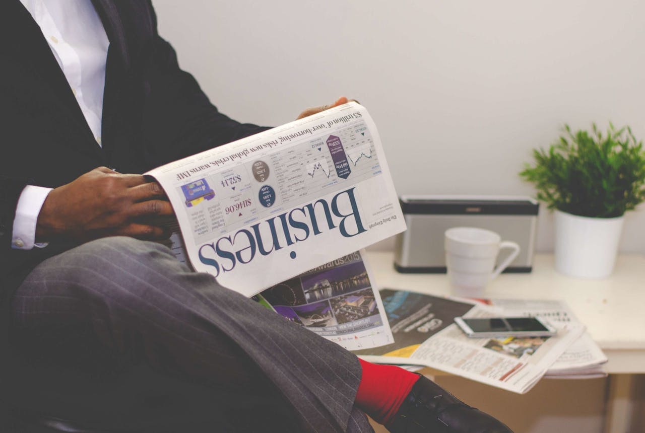 heros-img Businessman reading a financial newspaper at a desk, highlighting finance and commerce theme.